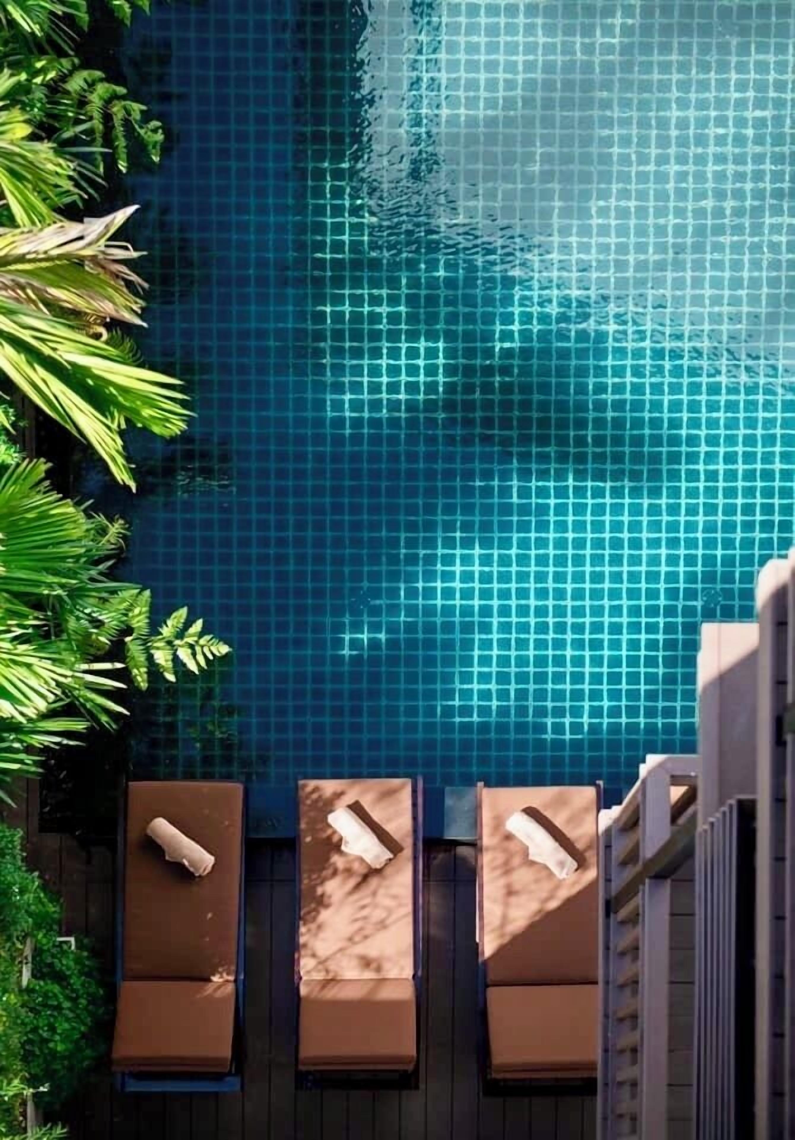 A swimming pool with tiled walls, surrounded by lounge chairs and greenery.