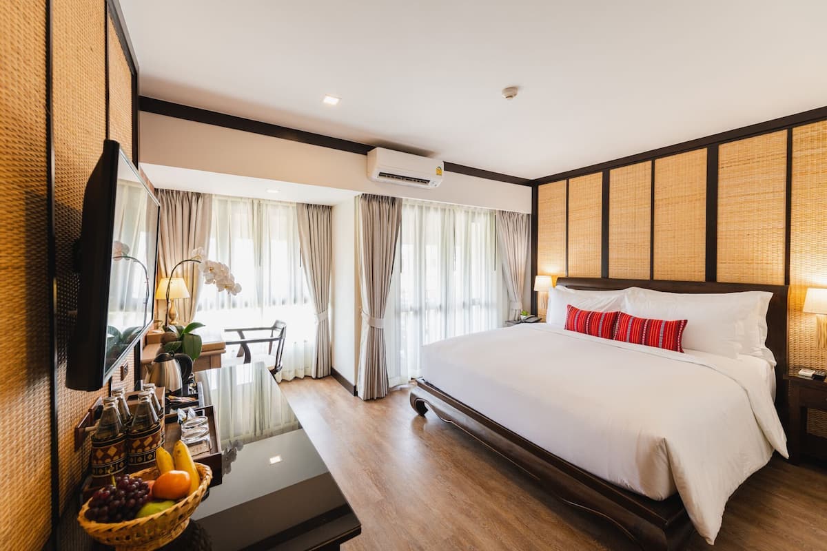 Hotelkamer met een groot bed, een televisie, een bureau met een computer, een fruitmand en uitzicht buiten door grote ramen.