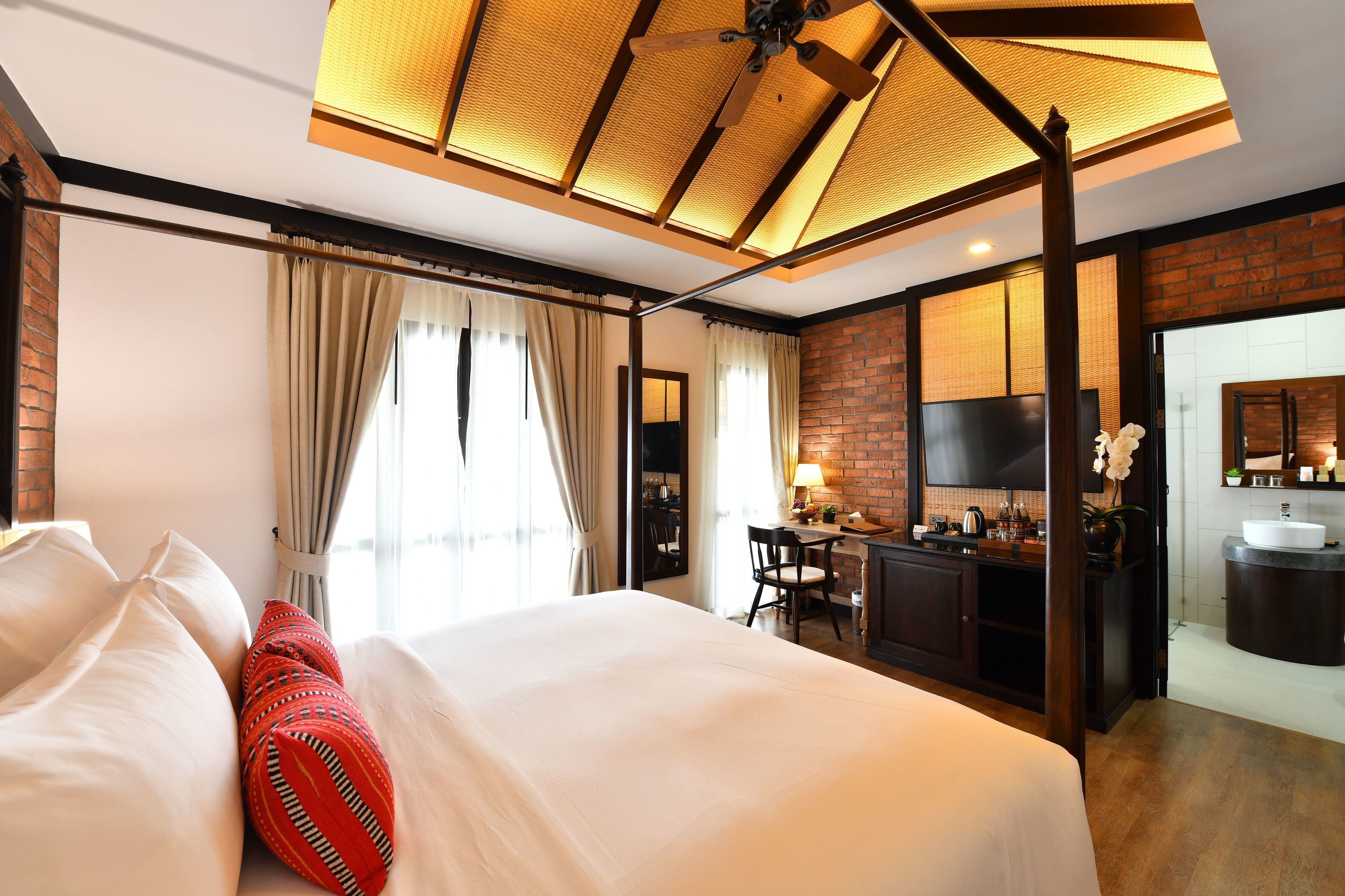 Una habitación de hotel con una cama grande, un escritorio con silla, una kitchenette y un baño con lavamanos.