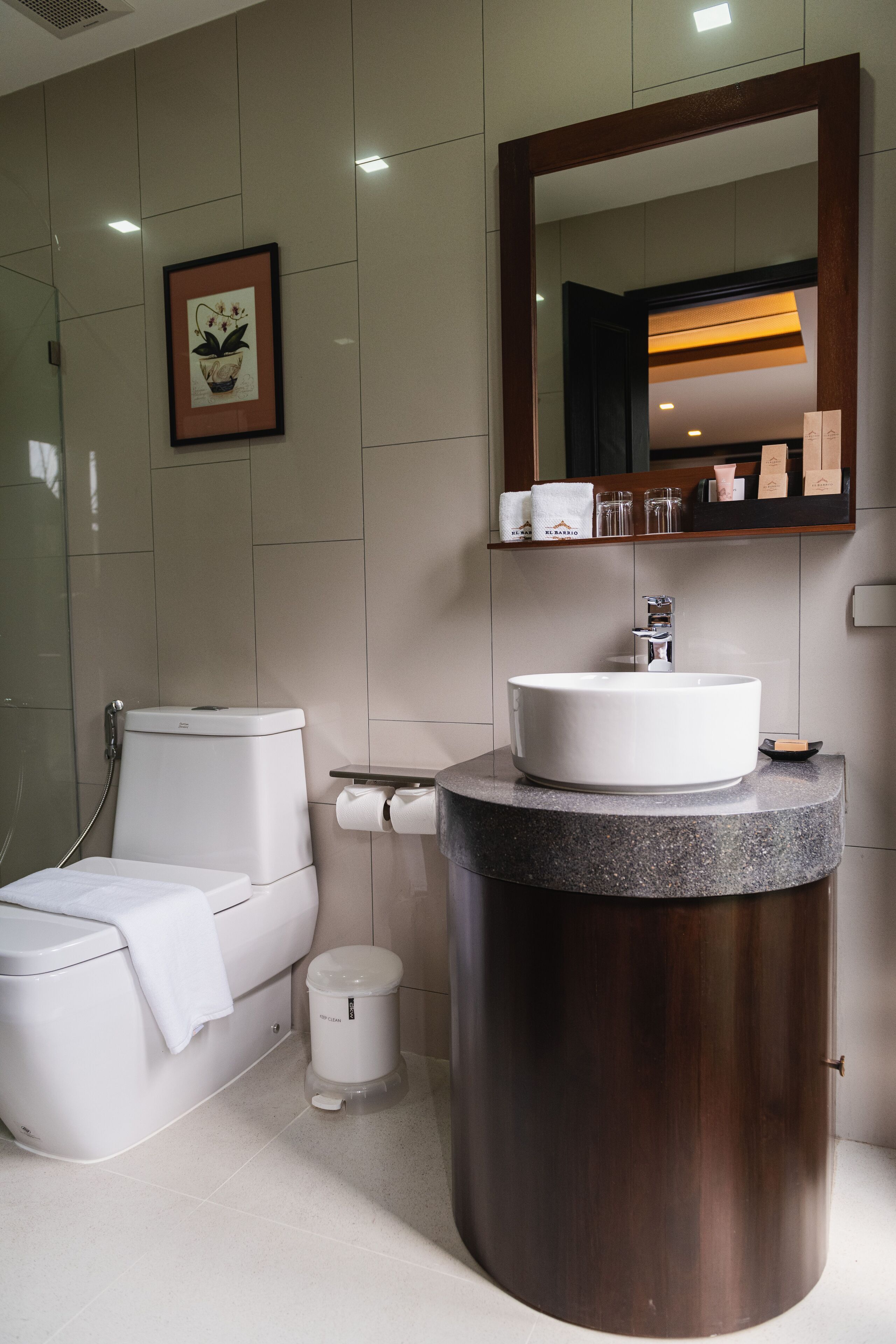 A modern bathroom with a white toilet, a sink with a wooden vanity, a mirror, and a framed picture on the wall.