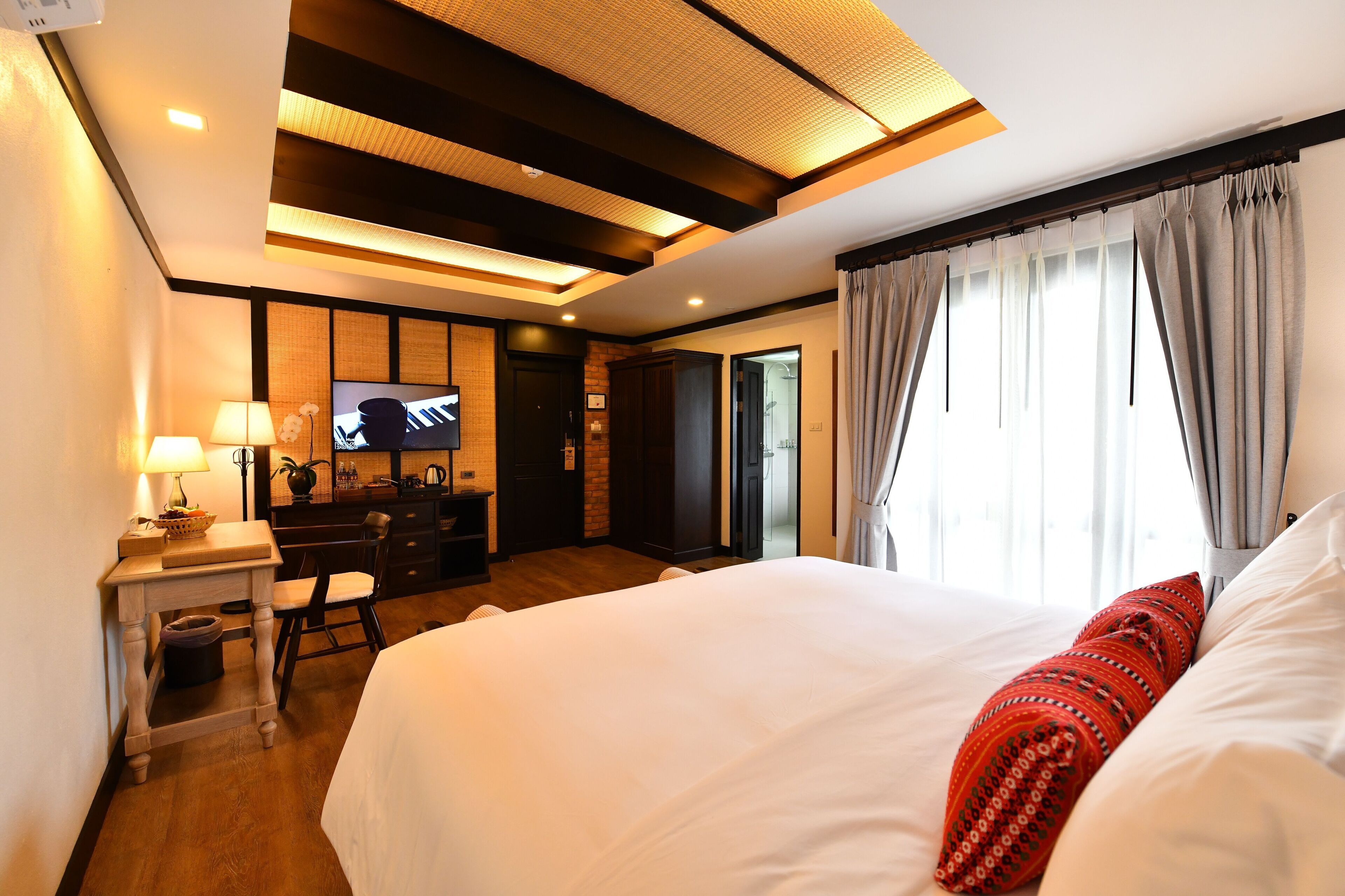 A hotel room with a large bed, a desk with a lamp, a television, and a view of the outdoors.