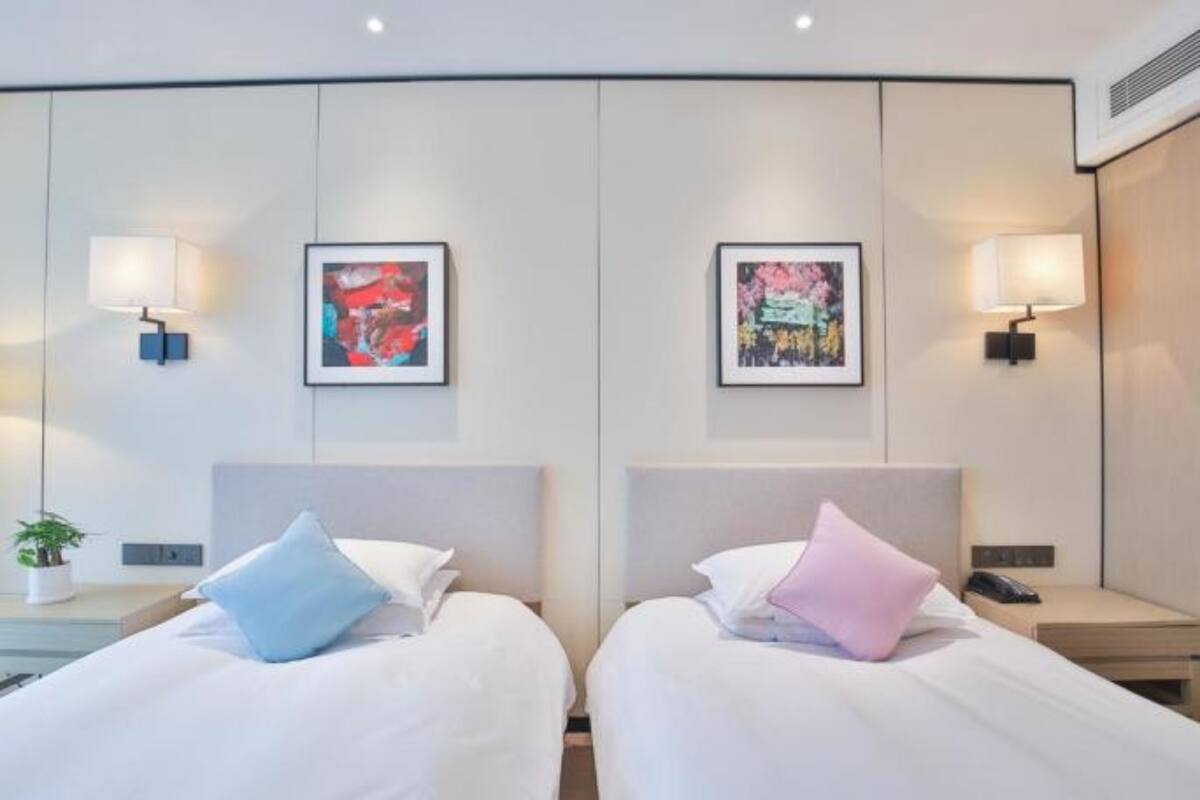 A hotel room with two beds, each with a pillow, a bedside table with a lamp, and a framed picture on the wall.