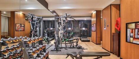 Un gimnasio moderno con diverso equipamiento de ejercicio, incluyendo mancuernas, bancos y máquinas de cardio.