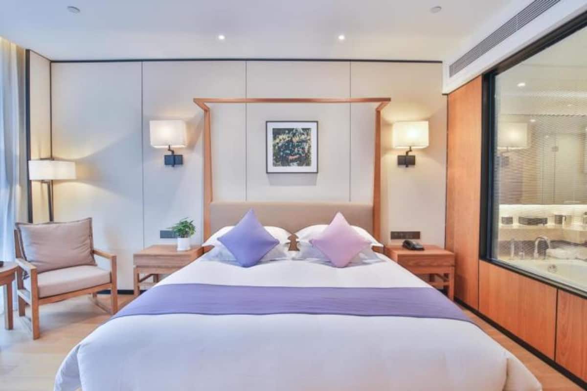 A modern hotel room with a large bed, two bedside tables, a chair, and a large window.