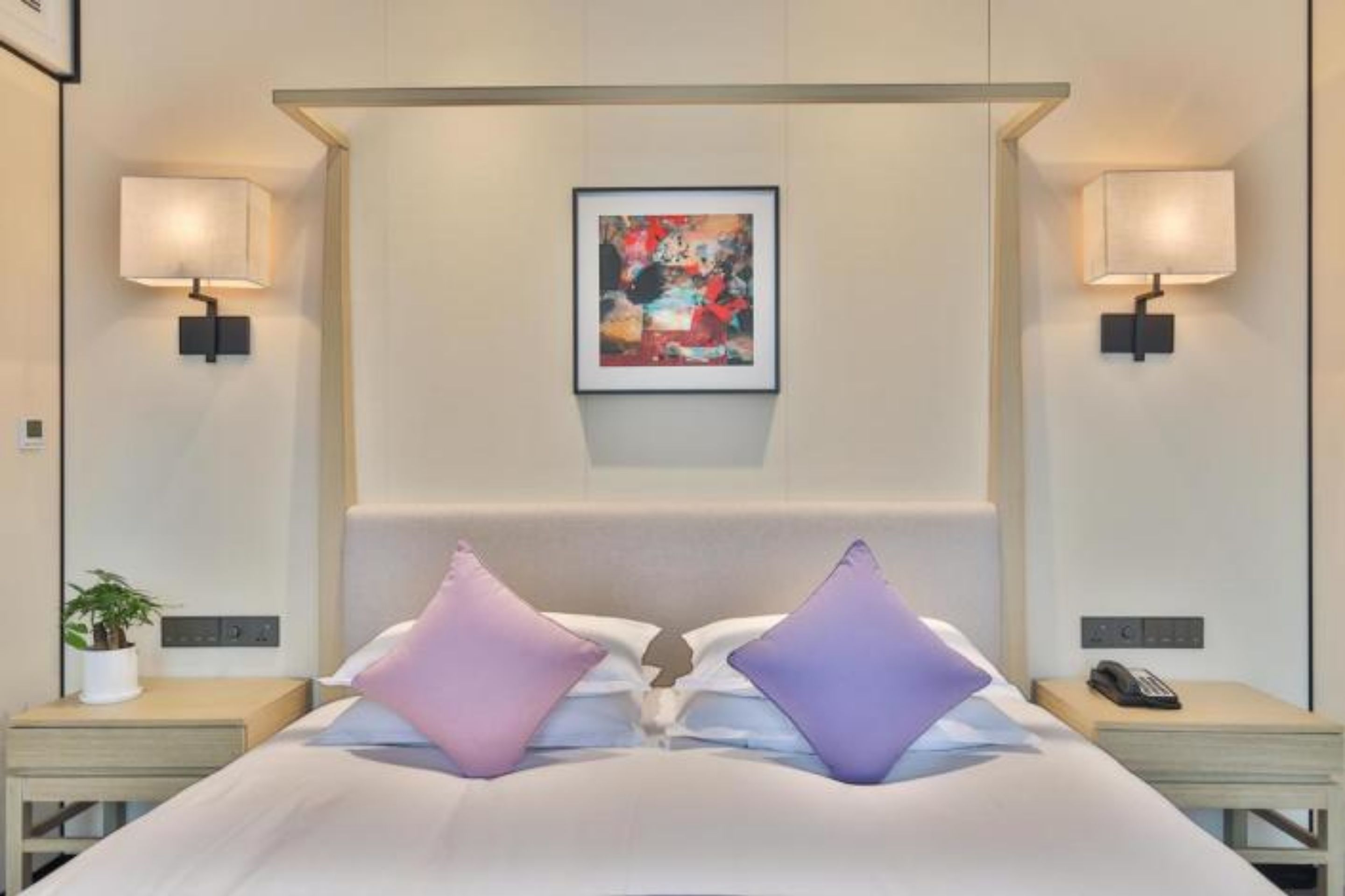 Camera d'albergo con un letto grande, due comodini, una lampada da comodino, un quadro appeso al muro e due applique.