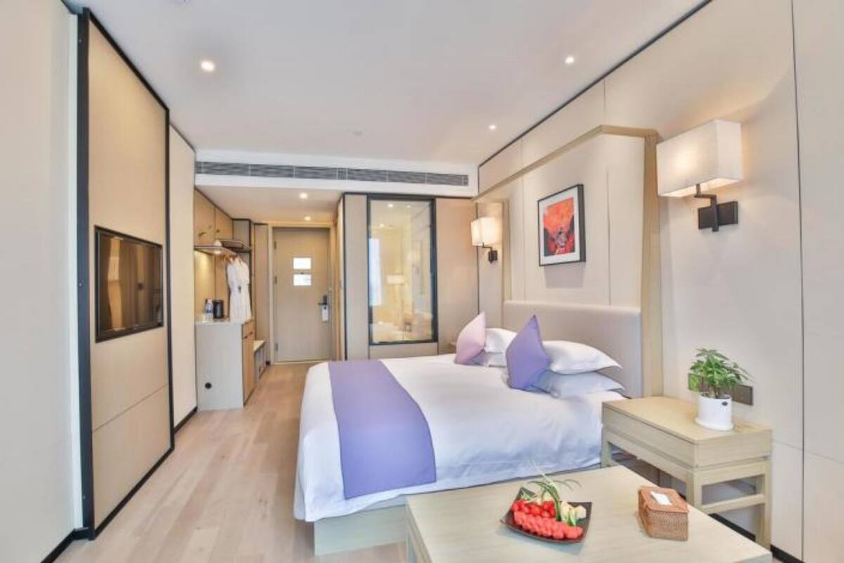 A modern hotel room with a large bed, bedside table, and a small table with fruit.