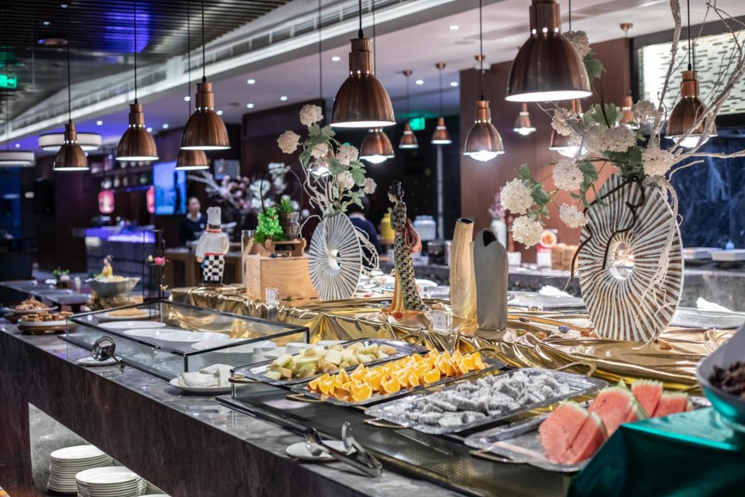 A buffet area with various food items, including fruits and desserts, and decorative elements like flowers and fans.