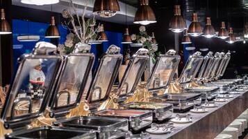 Una barra de buffet con múltiples estaciones de comida, cada una con un recipiente de vidrio transparente y una bandeja de metal para servir.