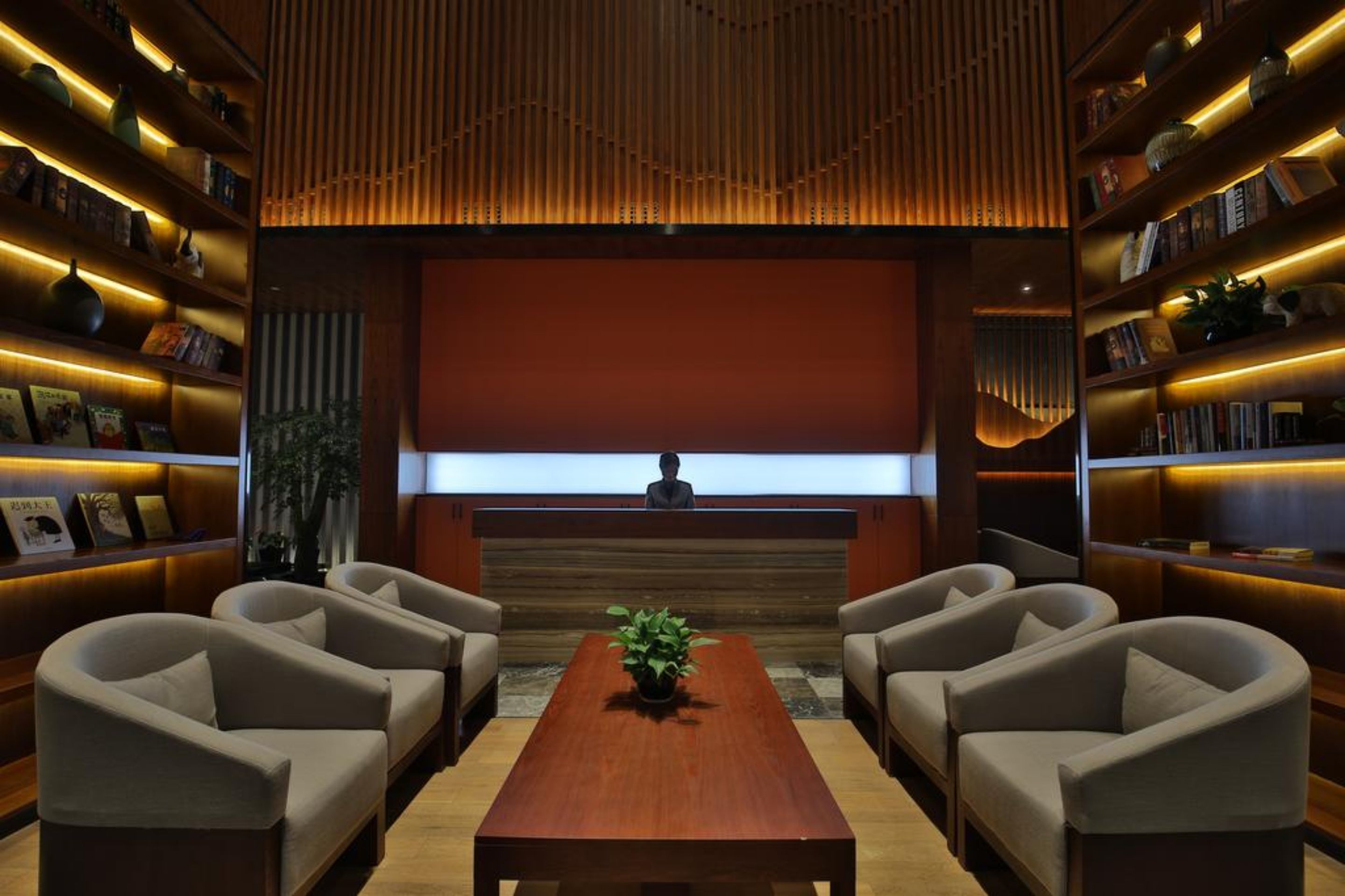A modern reception area with a wooden reception desk, two sofas, a coffee table, and bookshelves on either side.
