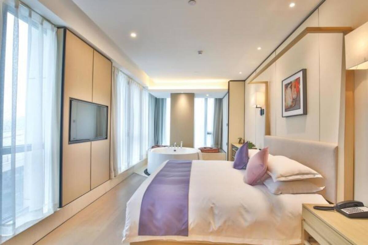 A modern hotel room with a large bed, a television, a desk, and a bathroom with a bathtub and sink.