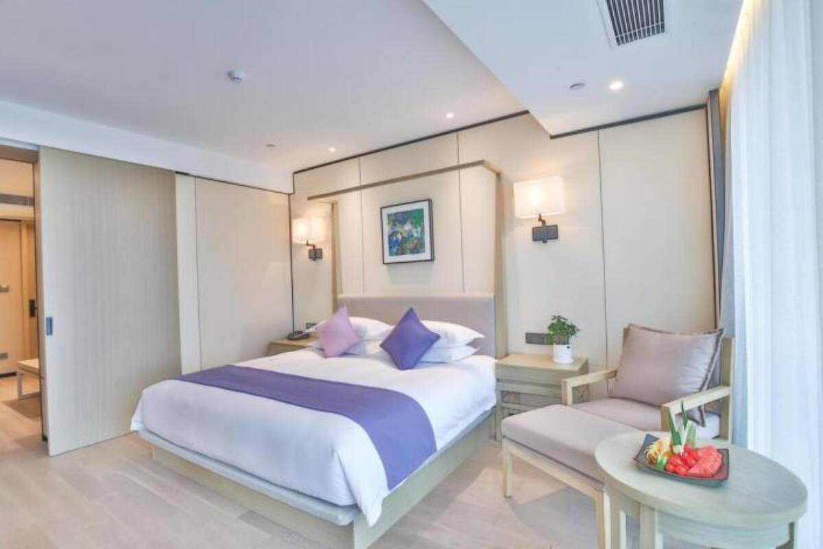 A modern hotel room with a large bed, bedside tables, a small seating area, and a view of the outdoors.