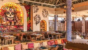 Un restaurant spacieux, doté de nombreuses tables et chaises, et décoré d’œuvres d’art colorées et de motifs floraux.