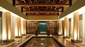 Un intérieur moderne agrémenté d’un élément aquatique central, d’un plancher en bois et de luminaires verticaux.