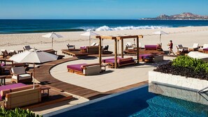 Un espace piscine aménagé dans un complexe hôtelier, avec des chaises longues en bois, des parasols et une vue sur l’océan.