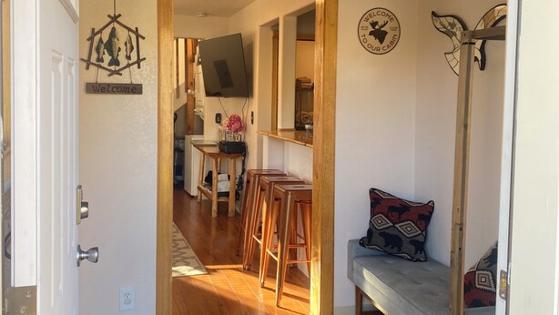 A cozy interior with a wooden door leading to a dining area, a bench, and a wall-mounted light fixture. - Alaskan Adventure Cabin (Sterling)