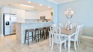 Une cuisine moderne avec des meubles blancs, un îlot central doté de tabourets et une table à manger avec des chaises.