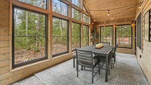 A wooden cabin interior with large windows, a dining table, and chairs.