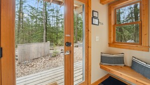 A wooden cabin with a glass door leading to a deck, a bench with cushions, and framed certificates on the wall.