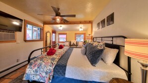 A bedroom with a bed, a ceiling fan, a window, and a lamp.