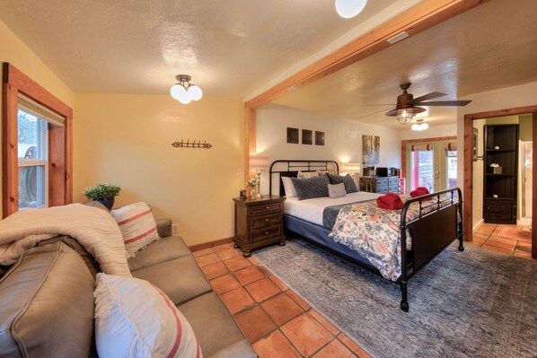 A bedroom with a bed, bedside table, lamp, and a view of the outside. - The Willow Cottage (Cali Cochitta ) (Moab)