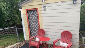 A small outdoor seating area with two red chairs and a small table, a decorative sign, and a welcome sign on a house. - Tinyhouse, Enchanted Cottage nestled in the backyard of the fenced in property. (Atlanta)