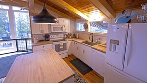 Een keuken met houten balken, witte kasten, een groot eiland, een magnetron, fornuis, spoelbak en een koelkast.