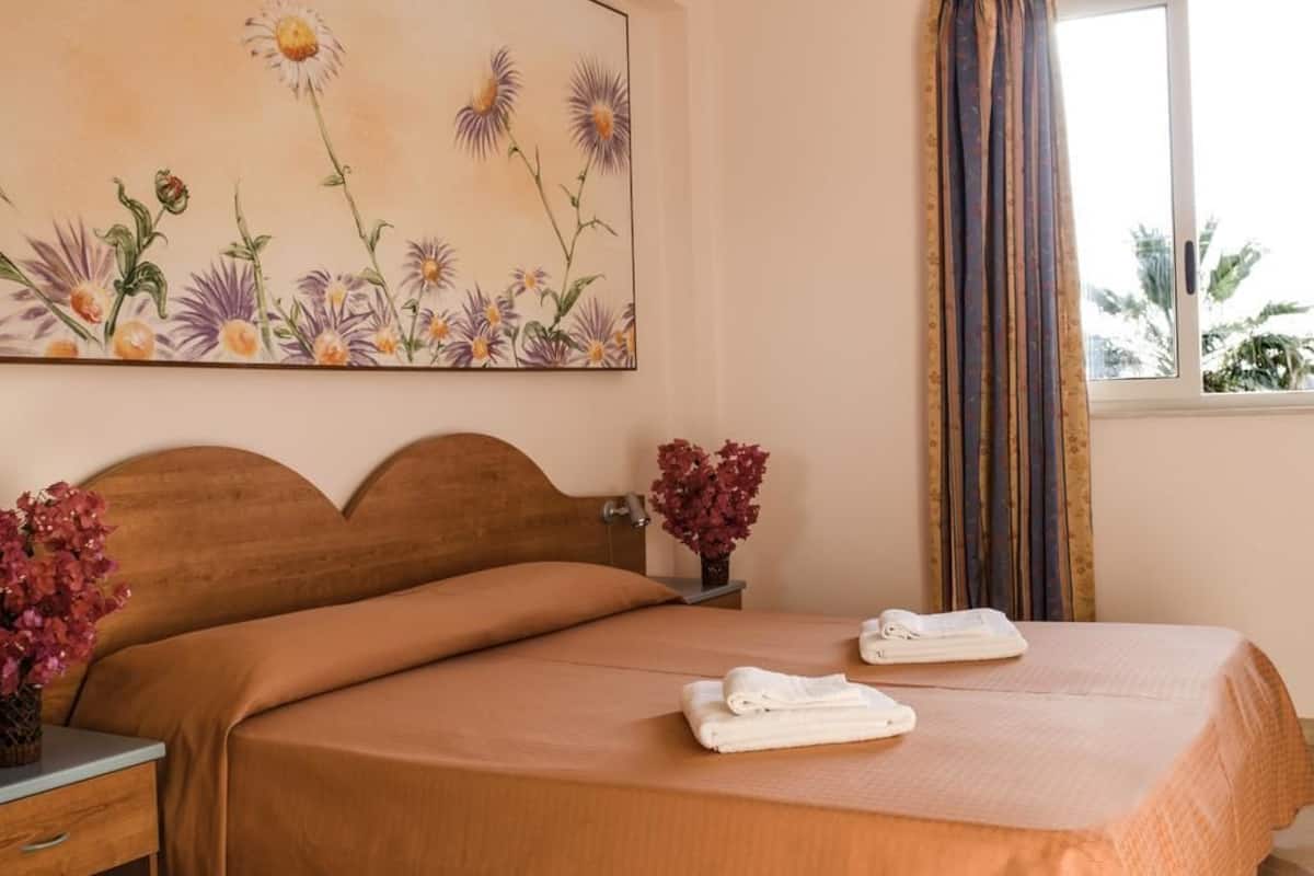 Uma cama bem arrumada com um cobre-leito marrom e duas toalhas brancas dobradas ao lado.