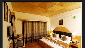 Ein Schlafzimmer mit Holzboden, einem Bett mit Kopfteil, einem Nachttisch mit Lampe und Vorhängen.