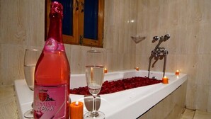 Eine Badewanne mit Rosenblüten, Kerzen und einer Flasche roséem Champagner.
