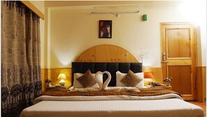 Ein ordentlich bezogenes Bett mit Kopfteil, zwei Nachttischlampen, einem gerahmten Bild an der Wand und einer Holztür.