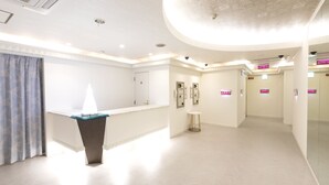 Een moderne hotelentree met een receptiebalie, een zithoek en een grote spiegelwand.