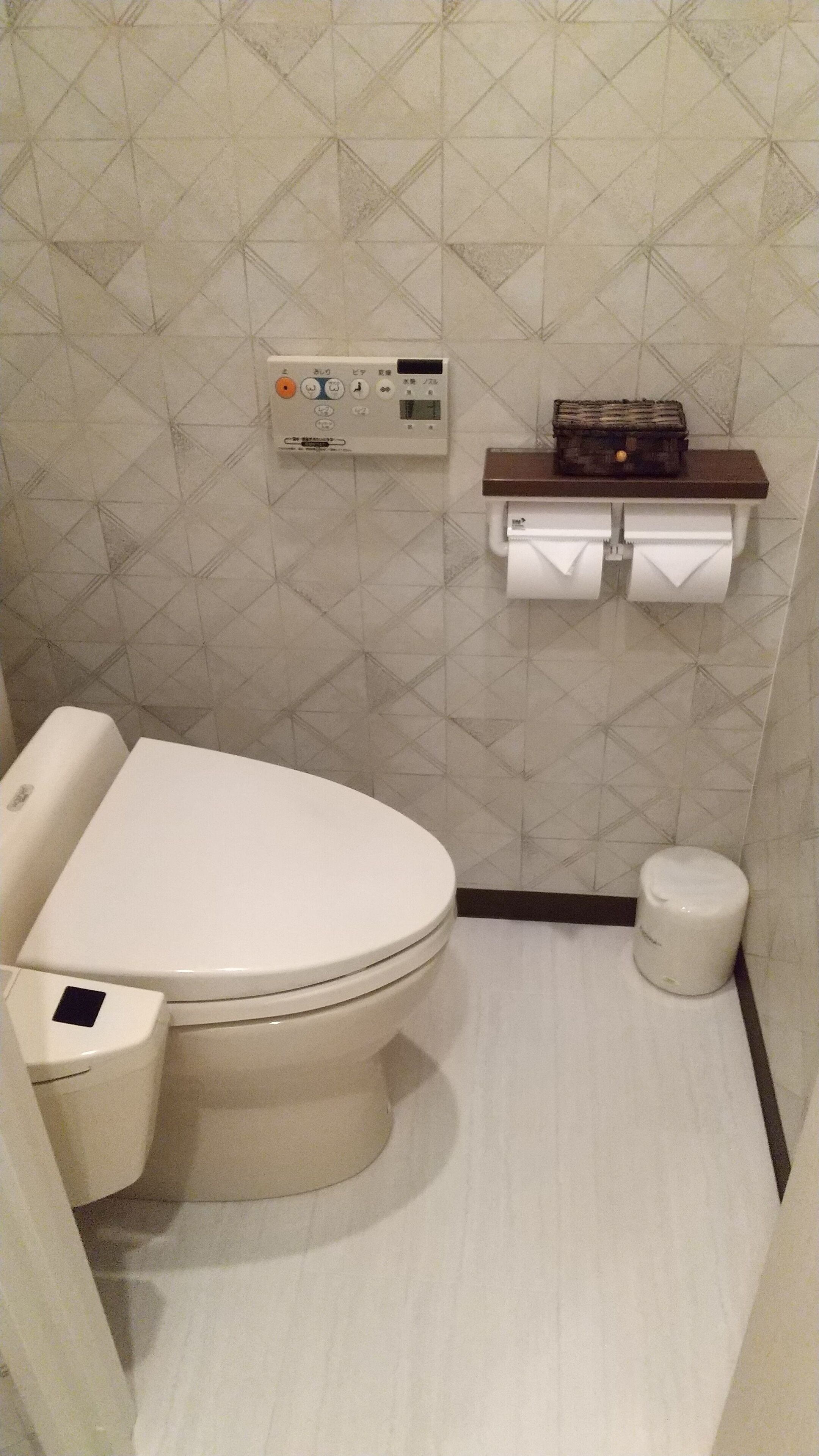 A bathroom with a toilet, a hand dryer, a paper towel dispenser, and a small trash bin.