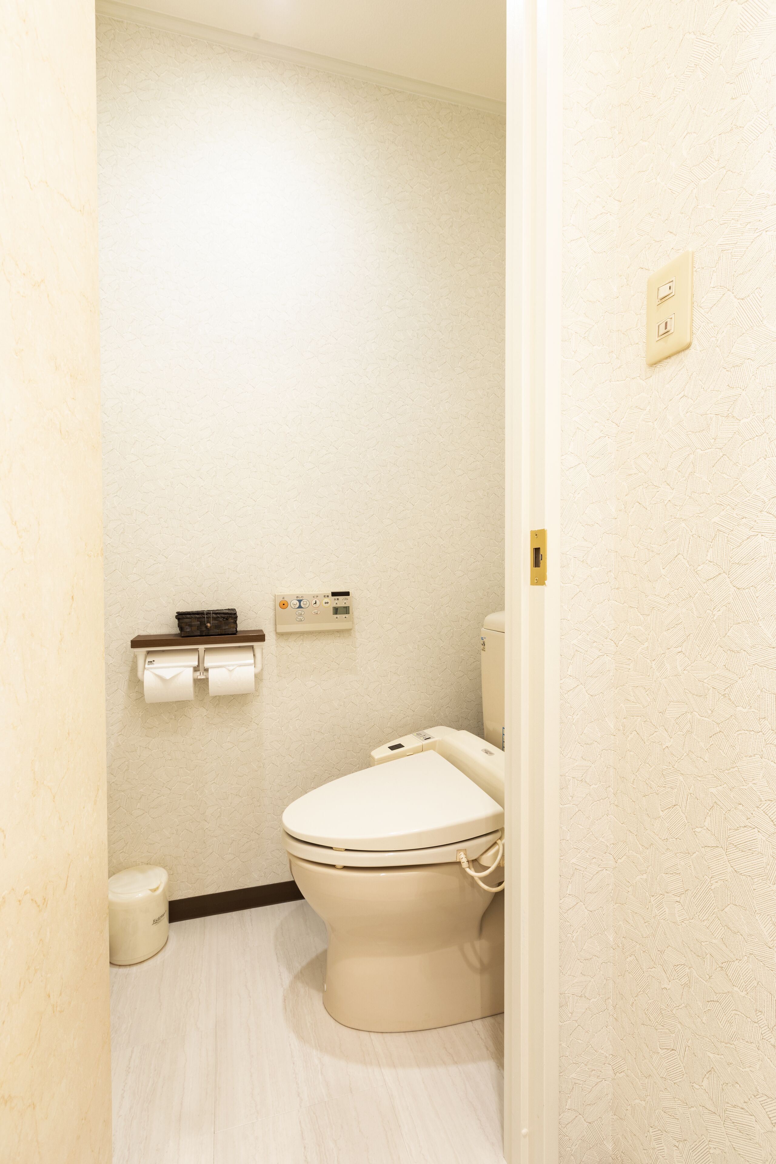 Un baño pequeño y limpio con inodoro, un dispensador de papel higiénico en la pared y un pequeño cubo de basura.