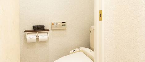 A small, clean bathroom with a toilet, a wall-mounted toilet paper holder, and a small trash bin.