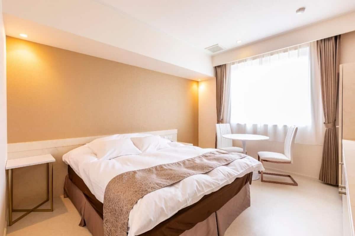 A hotel room with a bed, bedside table, chair, and a small round table.