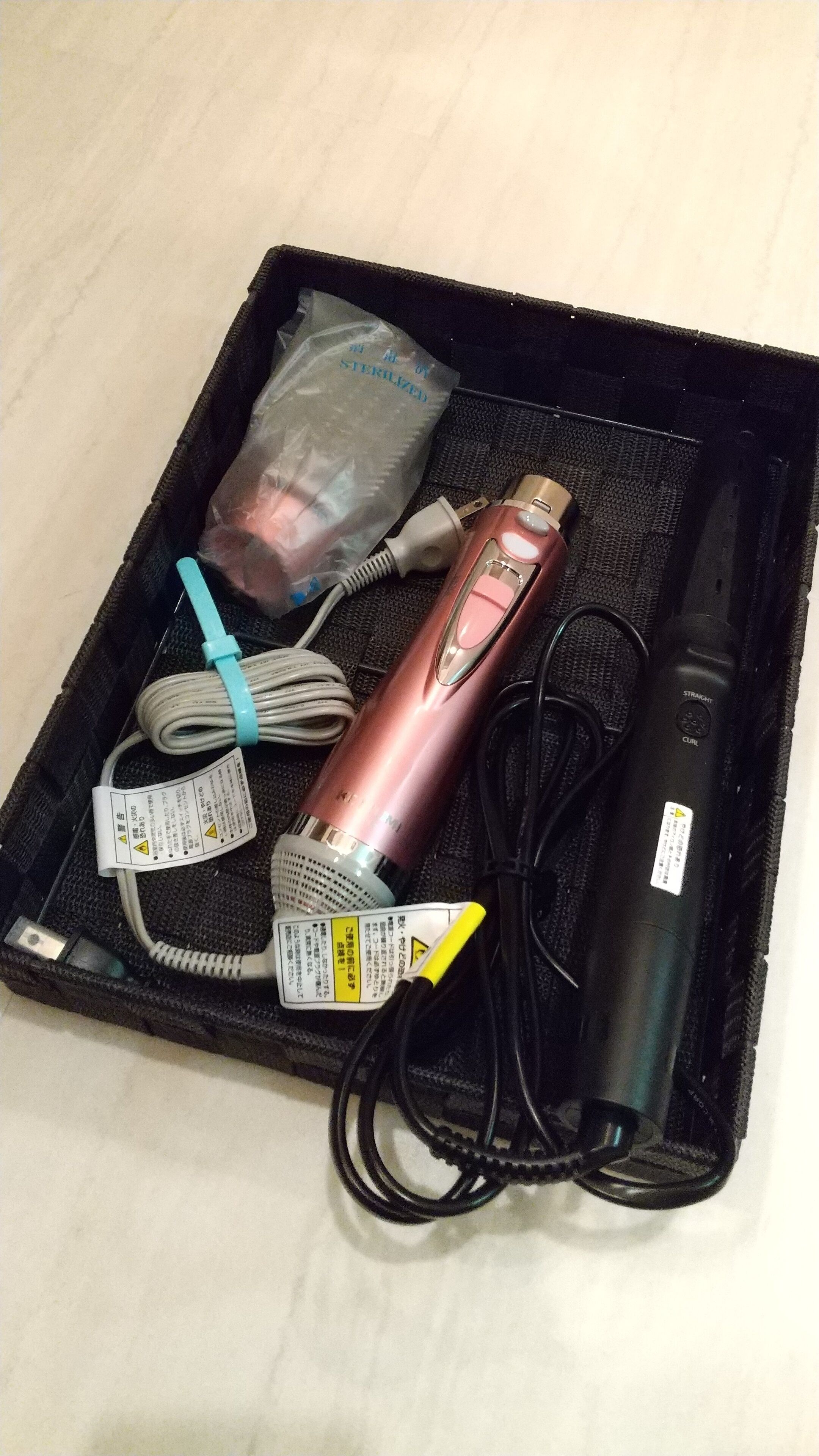 A black case containing a pink and black electronic device, a white charging cable, a USB cable, and a plastic bag labeled "STERILIZED".