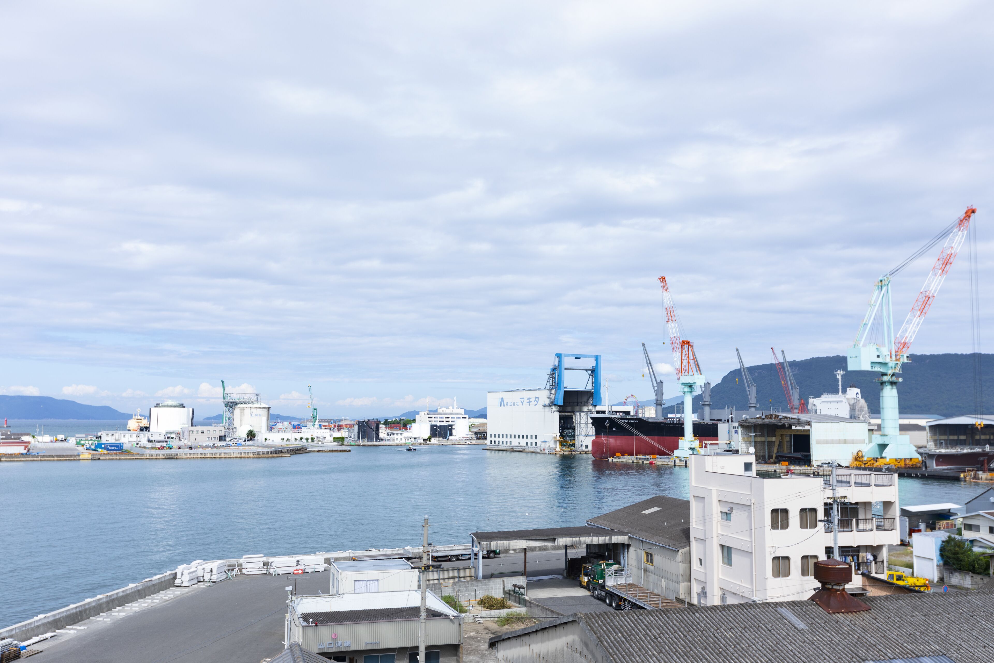 Un puerto con edificios industriales, grúas y un gran barco atracado.