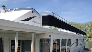 Una casa flotante blanca con terraza cubierta, ventanas y una pequeña zona de estar al aire libre.