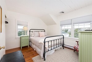A bedroom with a bed, a nightstand, a lamp, and a window with blinds. - Quintessential New England Home on Private Beach (Westerly)