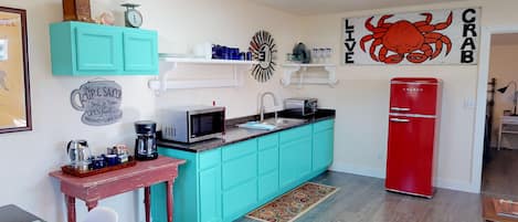 A compact kitchen with teal cabinets, a red refrigerator, a microwave, and a coffee maker.