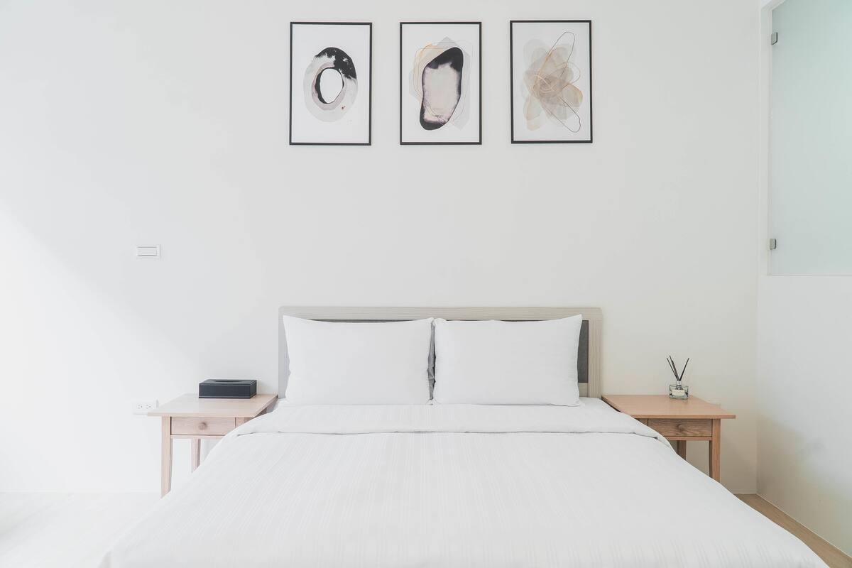 Ein schlicht eingerichtetes Hotelzimmer mit einem Bett, zwei Nachttischen und drei gerahmten abstrakten Kunstwerken an der Wand.