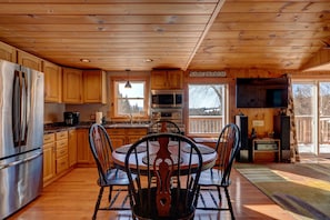 A wooden cabin kitchen with a dining table and chairs, a refrigerator, microwave, and a large window overlooking a lake. - Camp Coös - mountain and lake views with ATV/snowmobile trail access (Pittsburg)