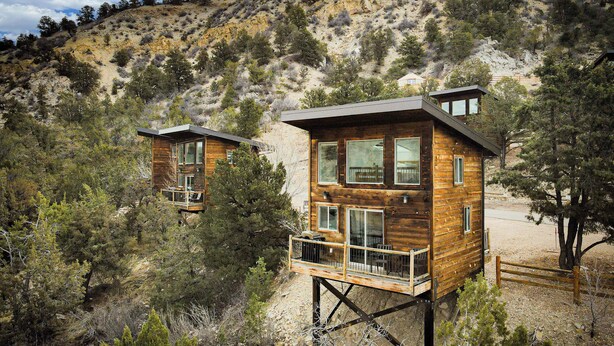 Dos cabañas de madera con balcones, ubicadas en una zona montañosa con vegetación escasa.