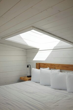 Een slaapkamer met dakraam, houten hoofdbord en witte beddengoed.