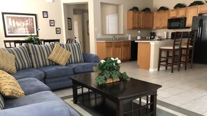 A living room with a blue sofa, a dark wooden coffee table, and a kitchen area with wooden cabinets and a microwave.