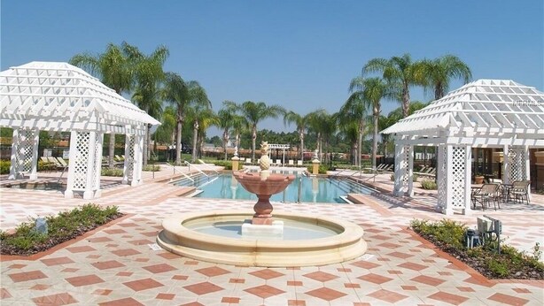 A pool area with two white gazebos, palm trees, and a central fountain.