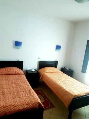 A room with two single beds, each with a matching nightstand. The room has white walls and a tiled floor. - Hotel Etrusco (Gherla)