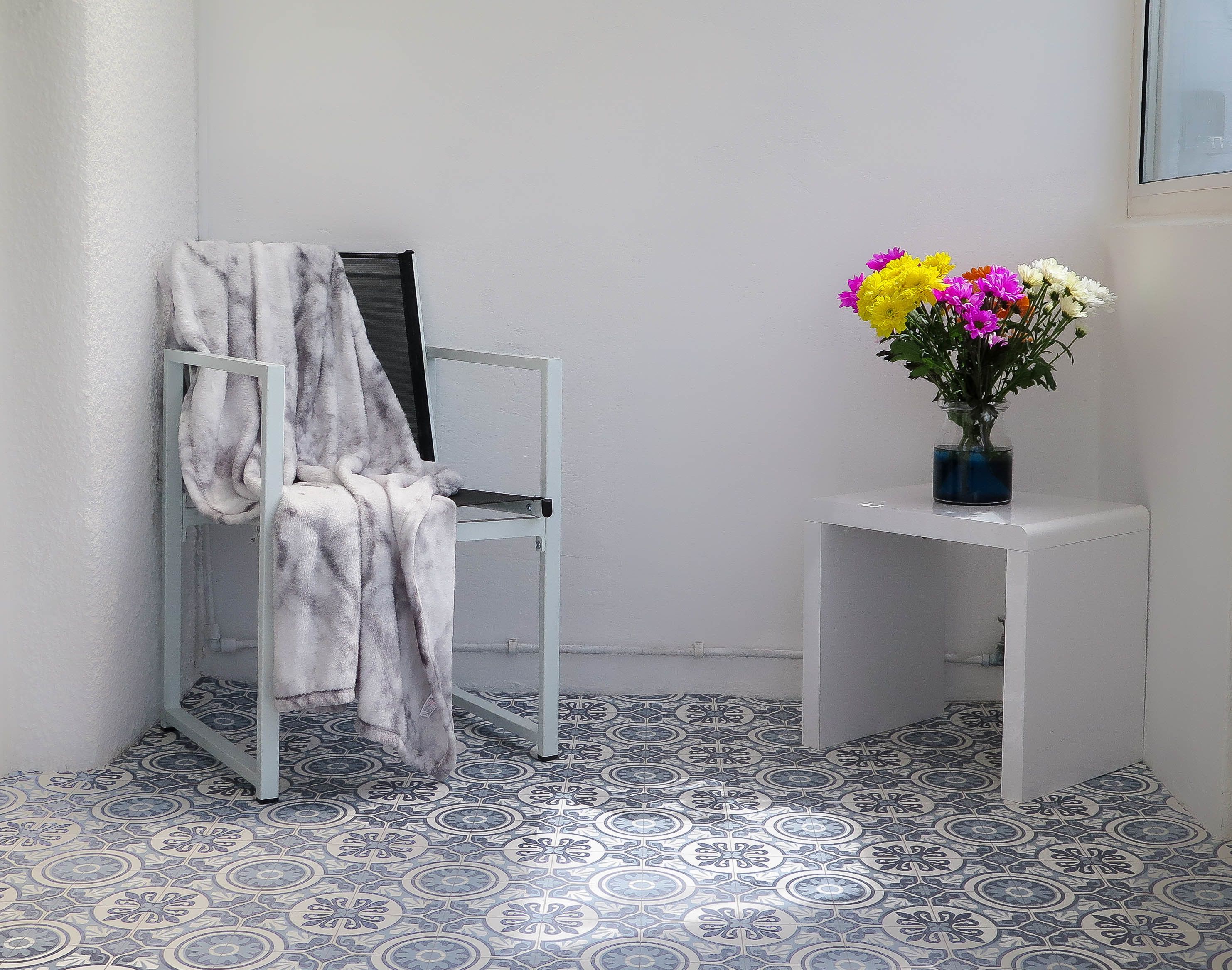 A bathroom with a white bathtub, a towel rack with a towel, a small white table with a vase of flowers, and patterned floor tiles.