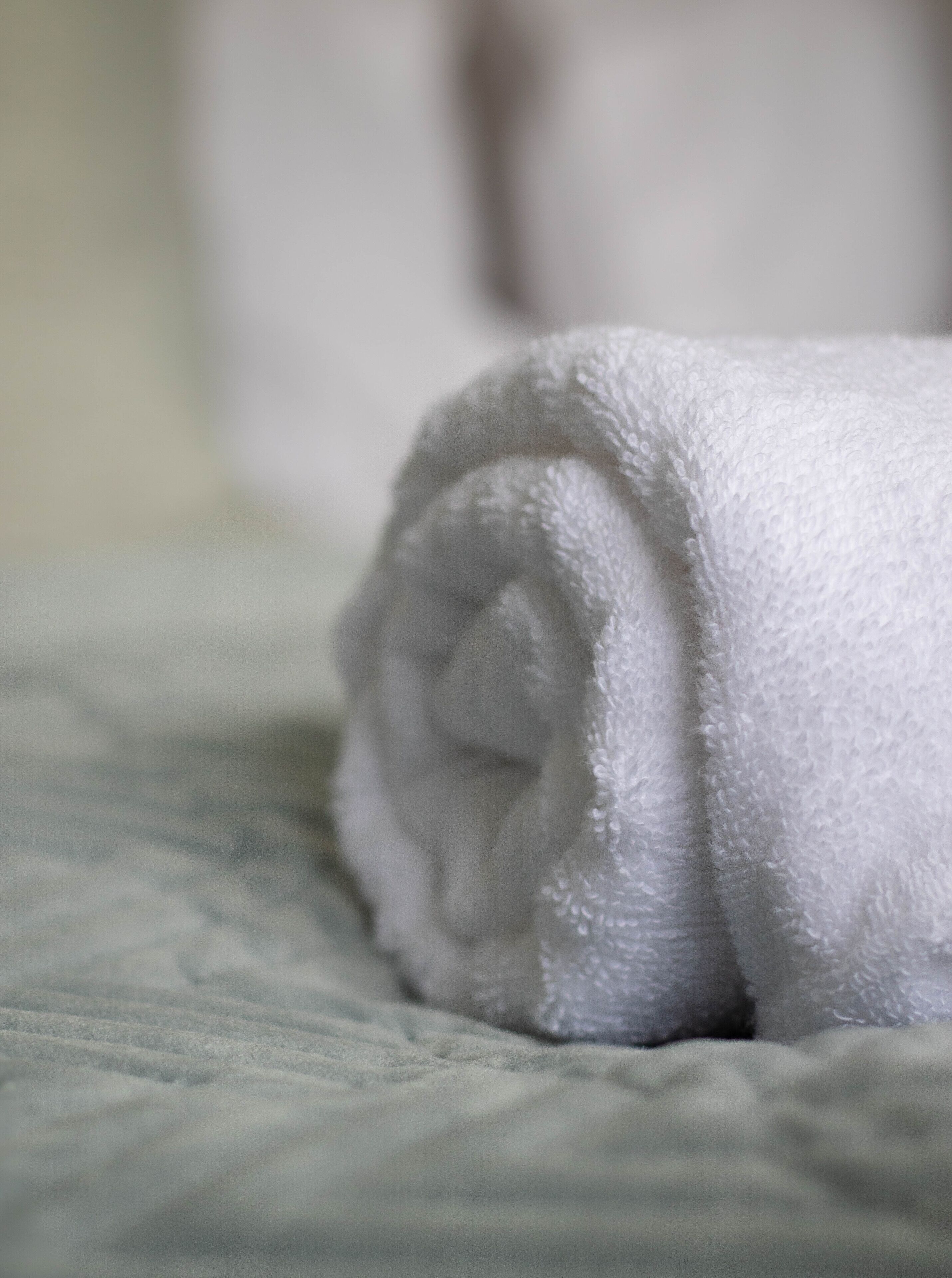 A neatly rolled white towel on a bed with a textured blanket.