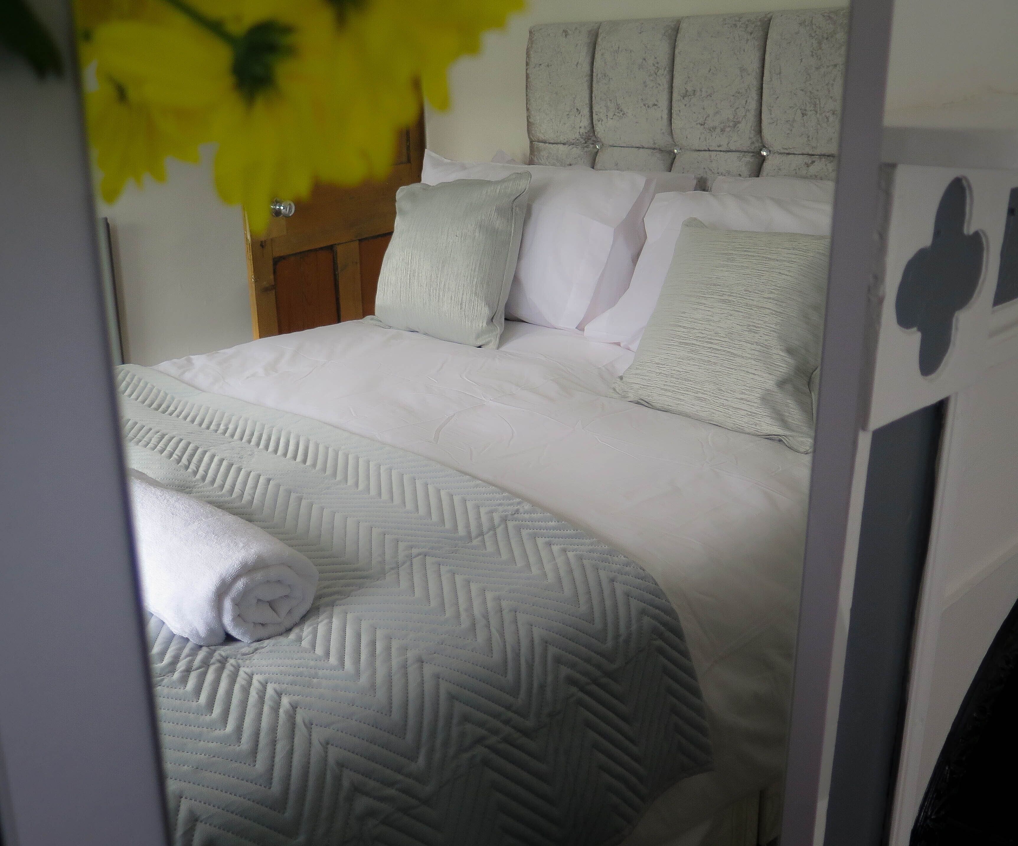 A neatly made bed with a patterned bedspread and pillows, a wooden headboard, and a door with a handle.